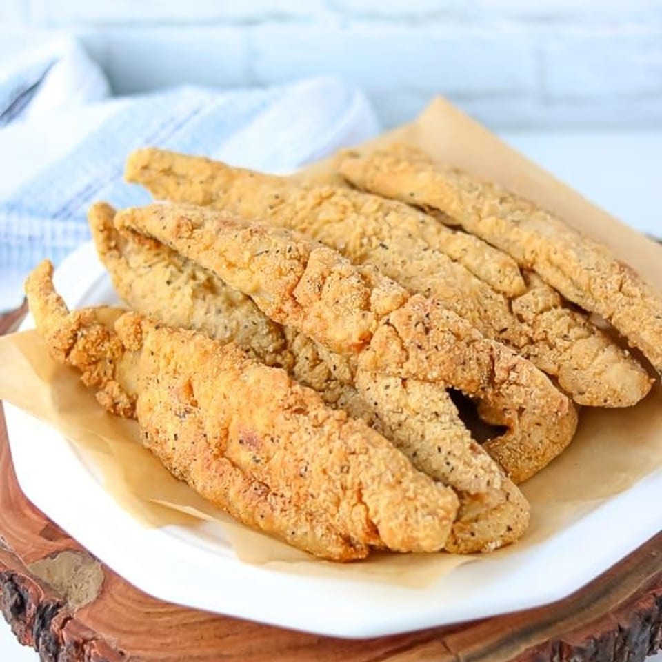 Plate of golden-brown breaded fried strips served on parchment over a rustic wooden slab.