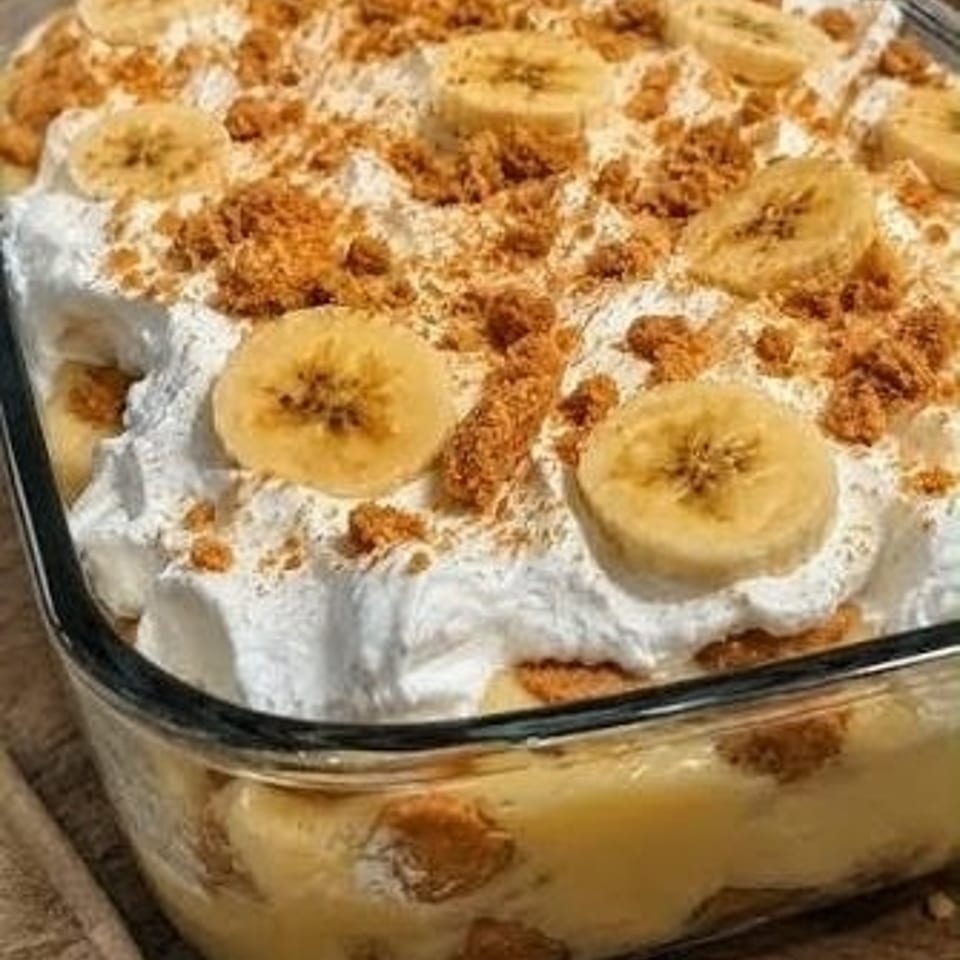 Glass dish of banana pudding layered with whipped cream, banana slices, and crumbled cookies.