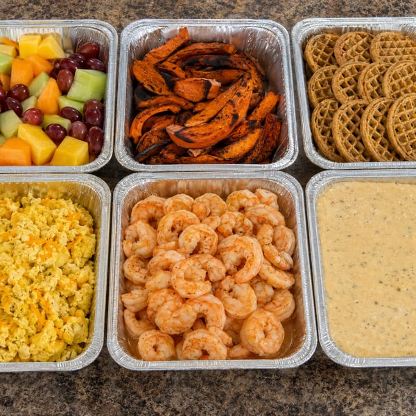 Assorted catering trays including fruit, shrimp, eggs, and waffles
